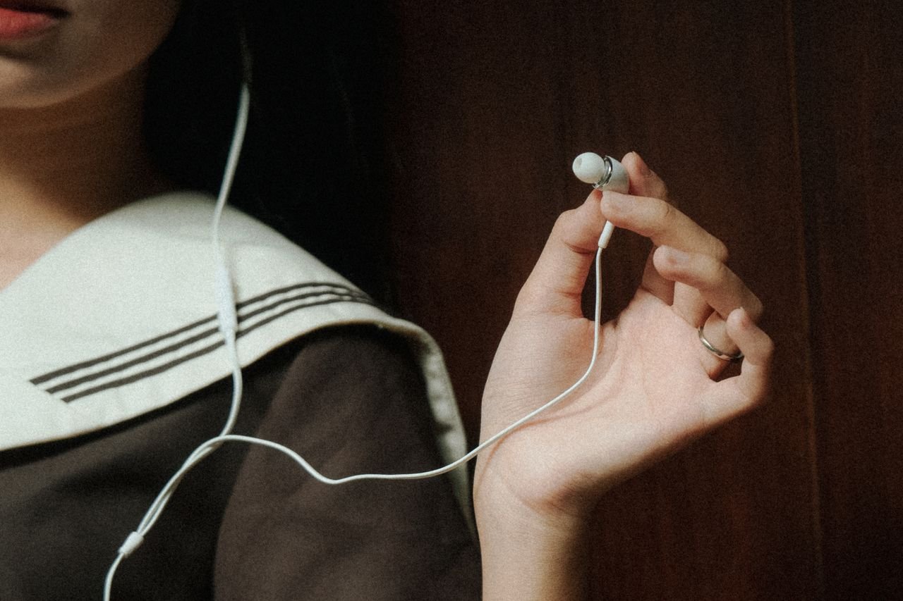 A close-up image of a hand holding earphones next to a person wearing navy attire, suggesting a relaxed mood.