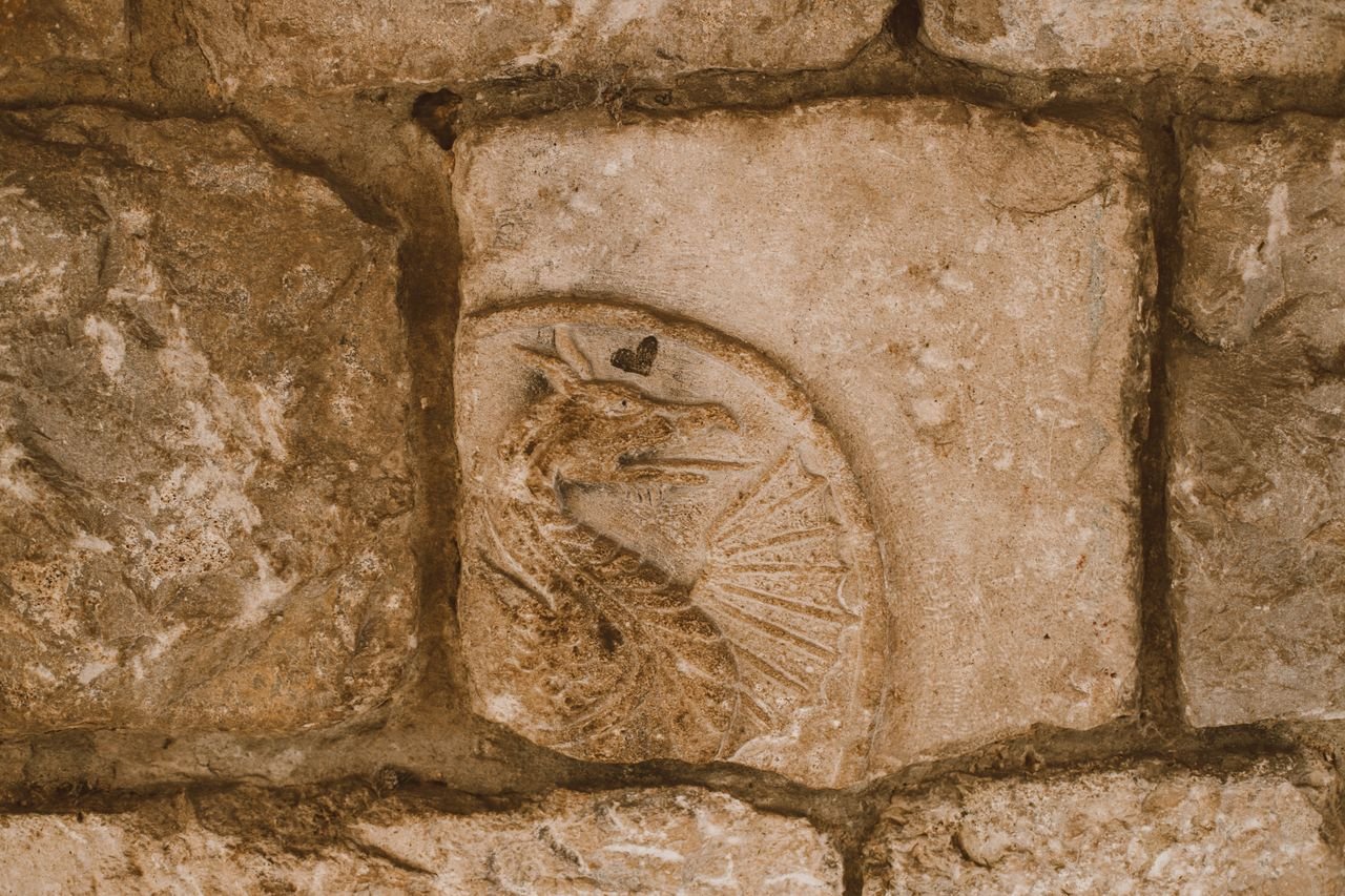 Close-up of an ancient dragon carving on textured stone, suggesting historical mystery.